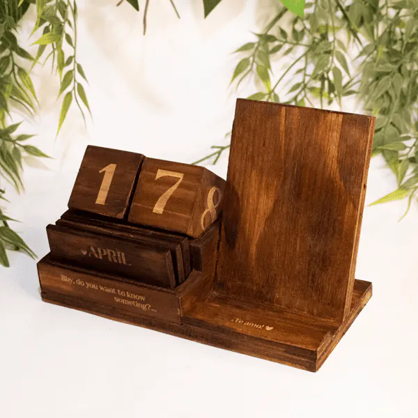 Calendario de Madera y Soporte Celular Calendario de Madera y Soporte para Celular, fabricado en madera natural con dimensiones de 12 cm de alto, 19 cm de largo y 8 cm de ancho. Incluye un calendario perpetuo con bloques grabados y un soporte integrado para celular. Personalizable con grabado láser, ideal para uso decorativo y funcional.