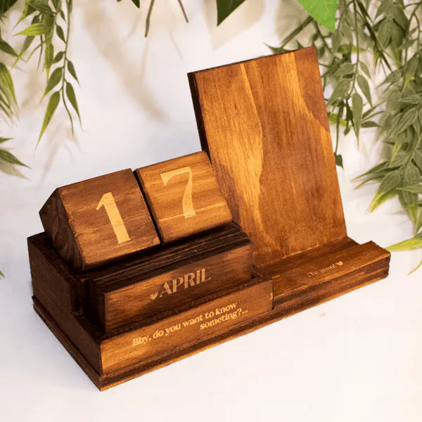 Calendario de Madera y Soporte Celular Calendario de Madera y Soporte para Celular, fabricado en madera natural con dimensiones de 12 cm de alto, 19 cm de largo y 8 cm de ancho. Incluye un calendario perpetuo con bloques grabados y un soporte integrado para celular. Personalizable con grabado láser, ideal para uso decorativo y funcional.