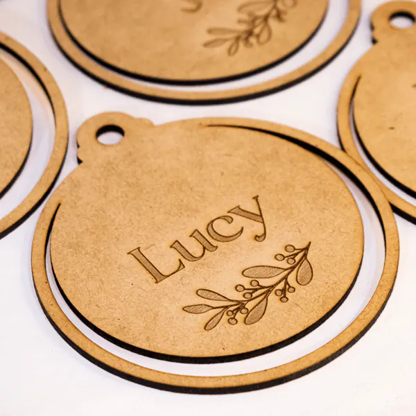 Esfera Navideña Personalizada en MDF | Trazos de Arte Esfera Navideña Personalizada en MDF, diseñada con precisión en dimensiones de 11 cm de alto, 10 cm de largo y 0,25 cm de ancho. Fabricada bajo pedido, incluye personalización mediante grabado láser que asegura un diseño detallado y único. Ideal como adorno decorativo para árboles, espacios festivos o como regalo simbólico y significativo durante la Navidad.