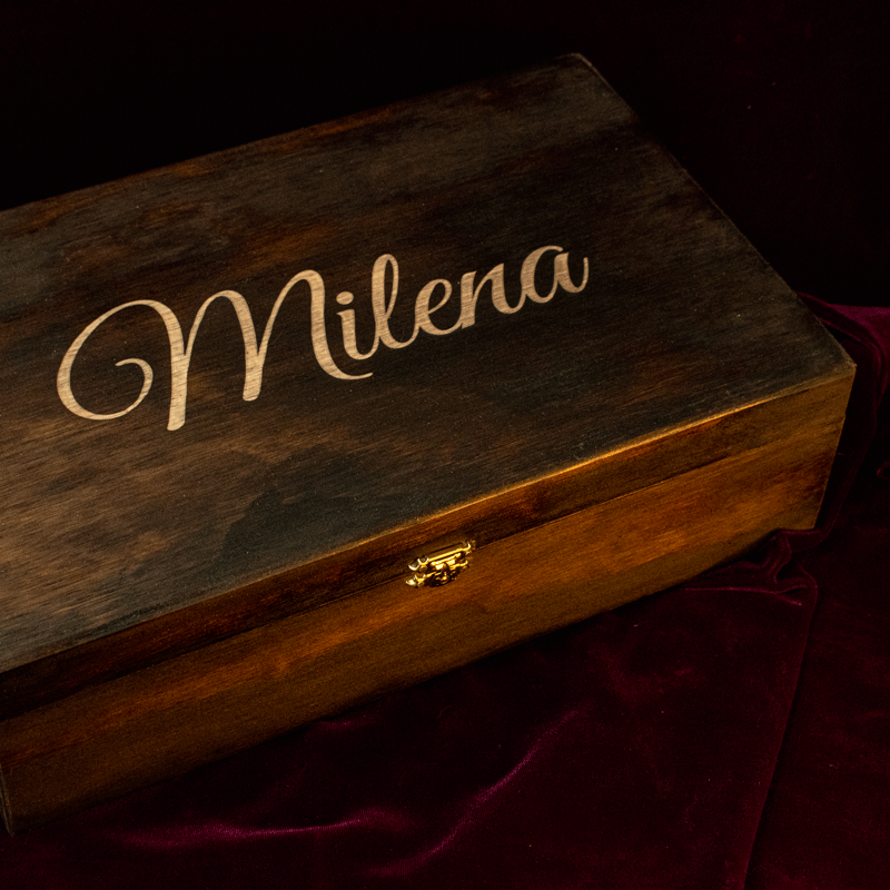 Una elegante caja rectangular de madera con un acabado oscuro y cálido. En la tapa, destaca el nombre 